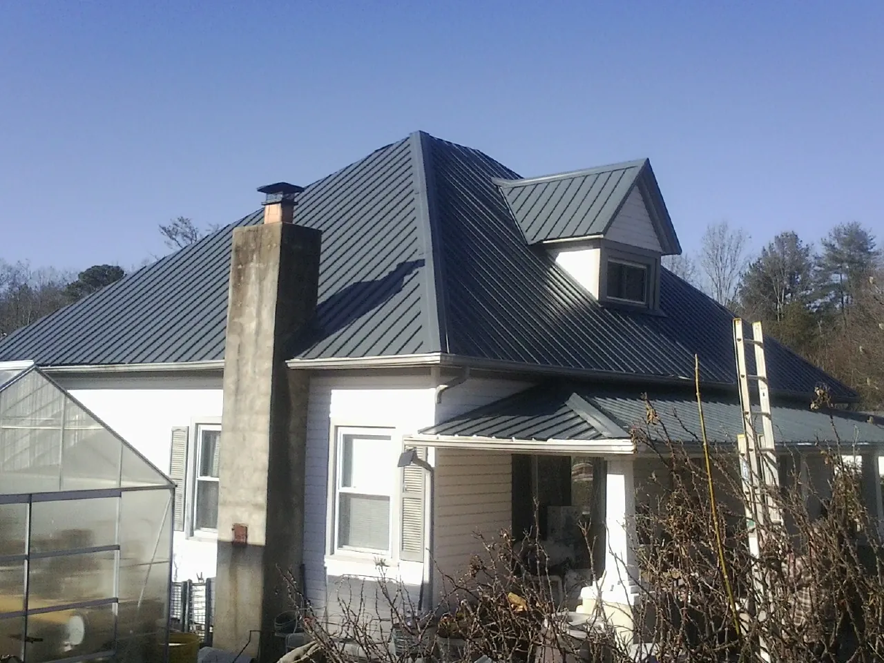Dark blue standing seam metal roof on a white farmhouse with dormer — Slate & Tile Roof Repair by Roofing Brothers in Cedarburg