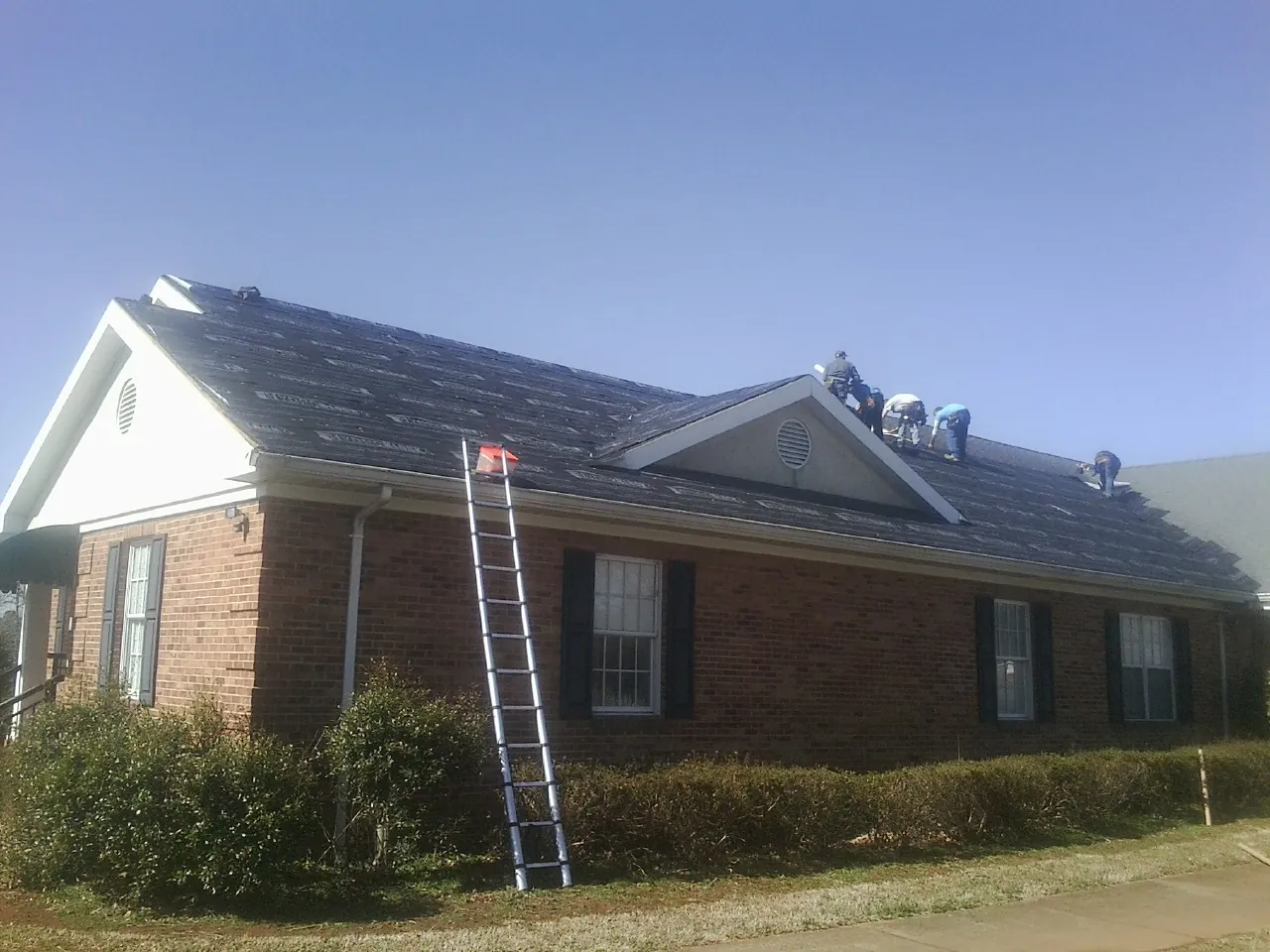 Crew tearing shingles off a brick ranch roof with a ladder set — Emergency Roof Repair work by our crew in Cedarburg