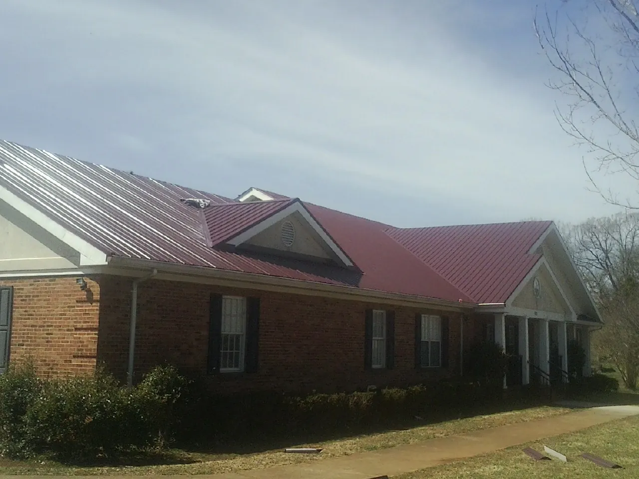 Red metal roof with gabled entries on a long brick building, from a Hail Damage Roof Repair job in Cedarburg