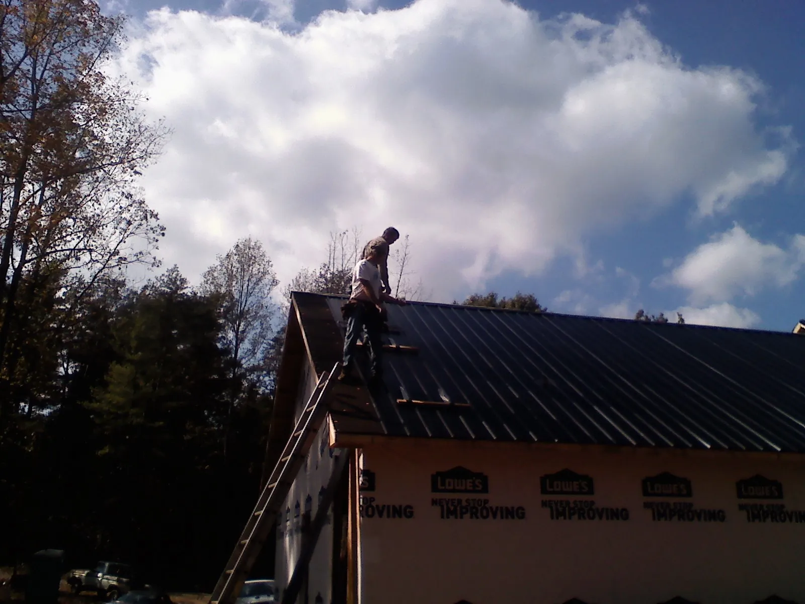 Roofer fastening dark metal panels high against a cloudy sky, from a Roof Inspection job in Cedarburg