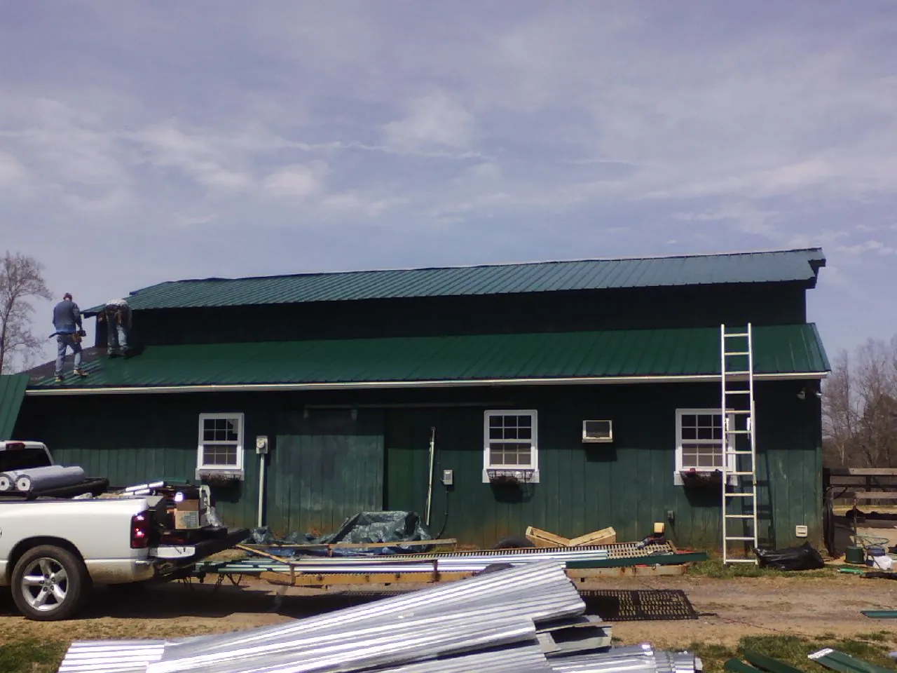 Crew installing green metal roofing on a large green barn in Cedarburg
